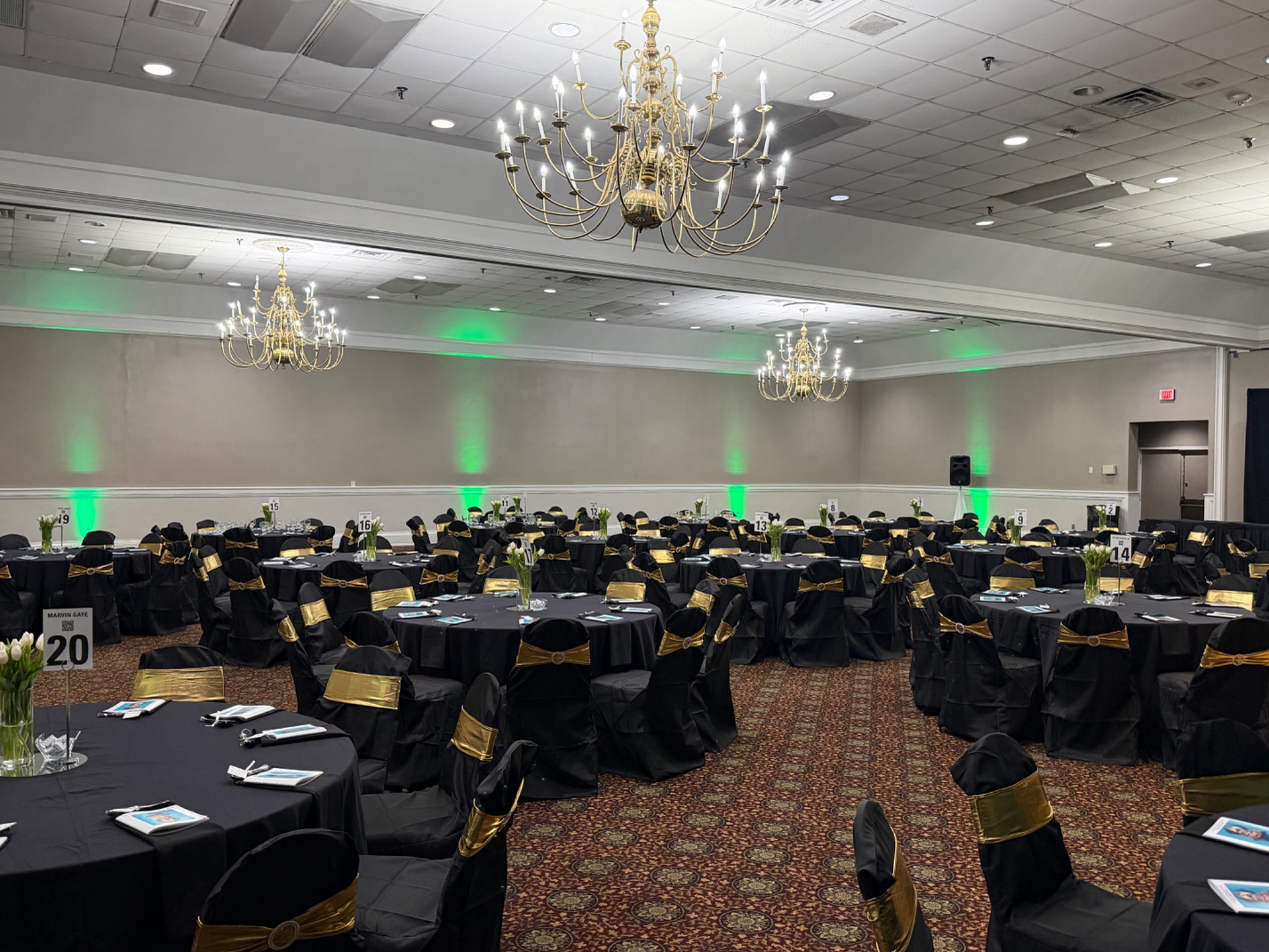 Large ballroom with banquet tables, chandeliers, and green uplighting