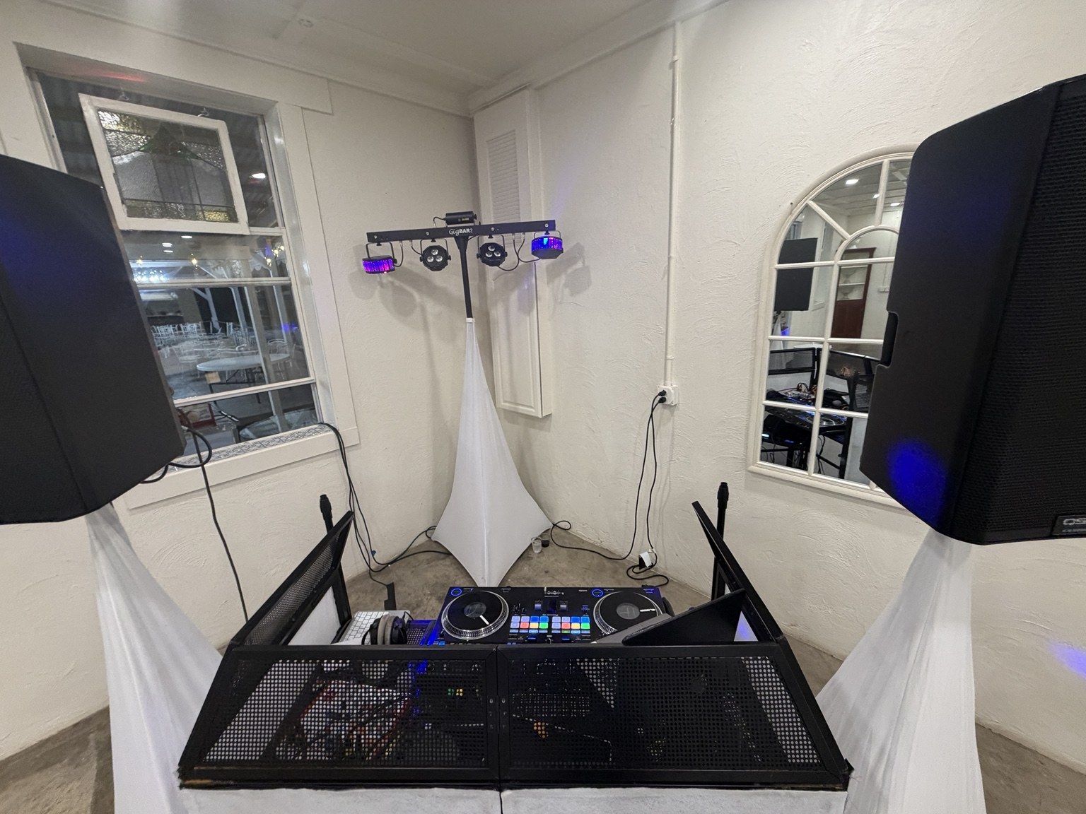 View from behind a DJ booth with speakers, lighting, and controller setup
