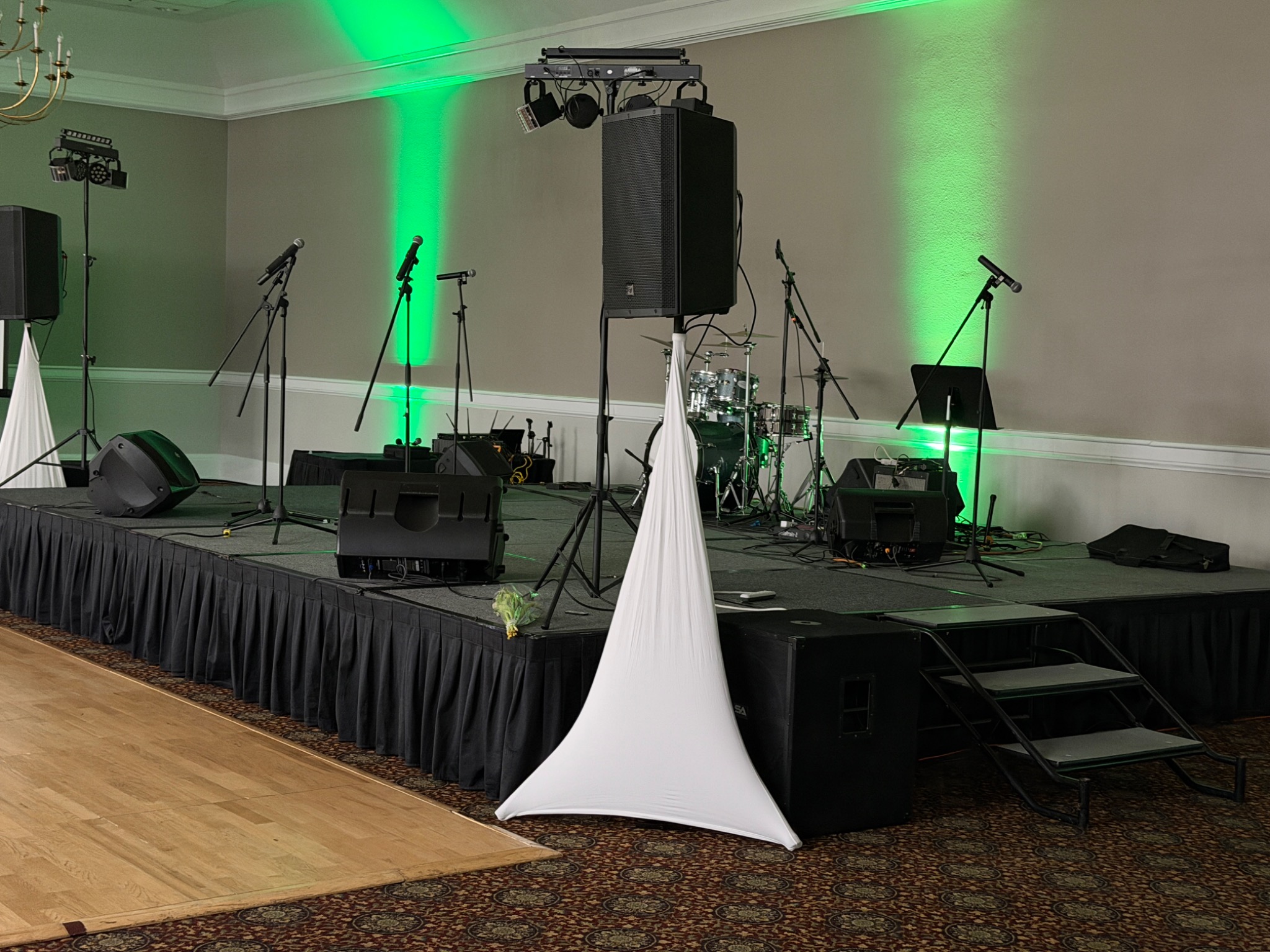 Indoor stage with drum kit, microphones, speaker stacks, and green uplighting