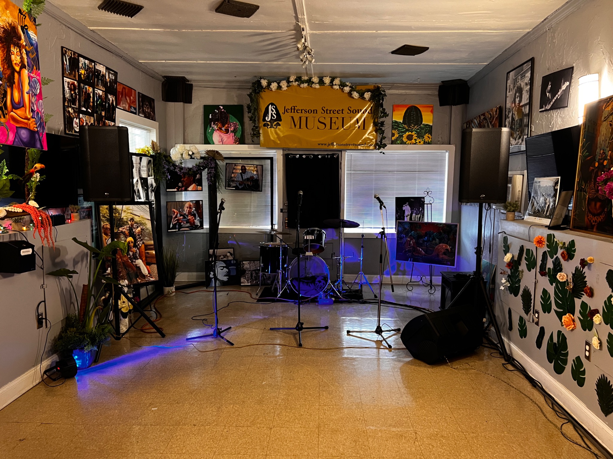 Small museum performance space with drum kit, speakers, and microphones